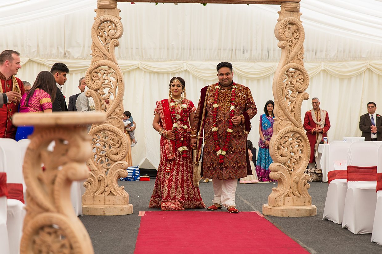 An Asian couple walking through an arch as their guests watch