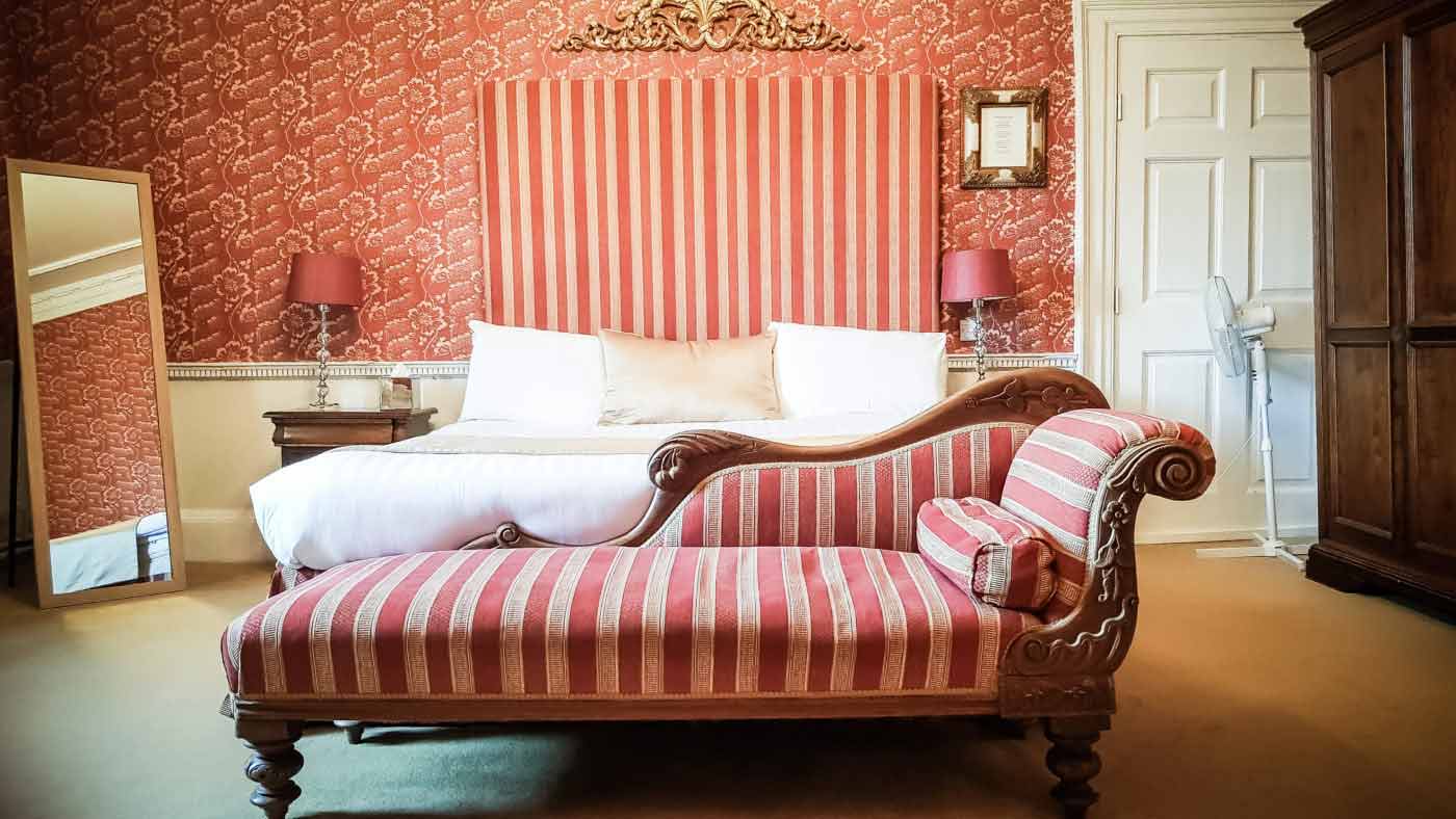 King sized bed with sofa in front of it. Accompanied by a mirror, lamp and dresser.