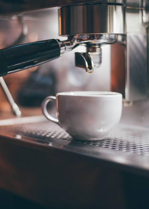 A cup placed under coffee machine handle waiting to be filled.