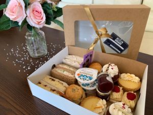 Take away afternoon tea in a box with pink roses in the background.