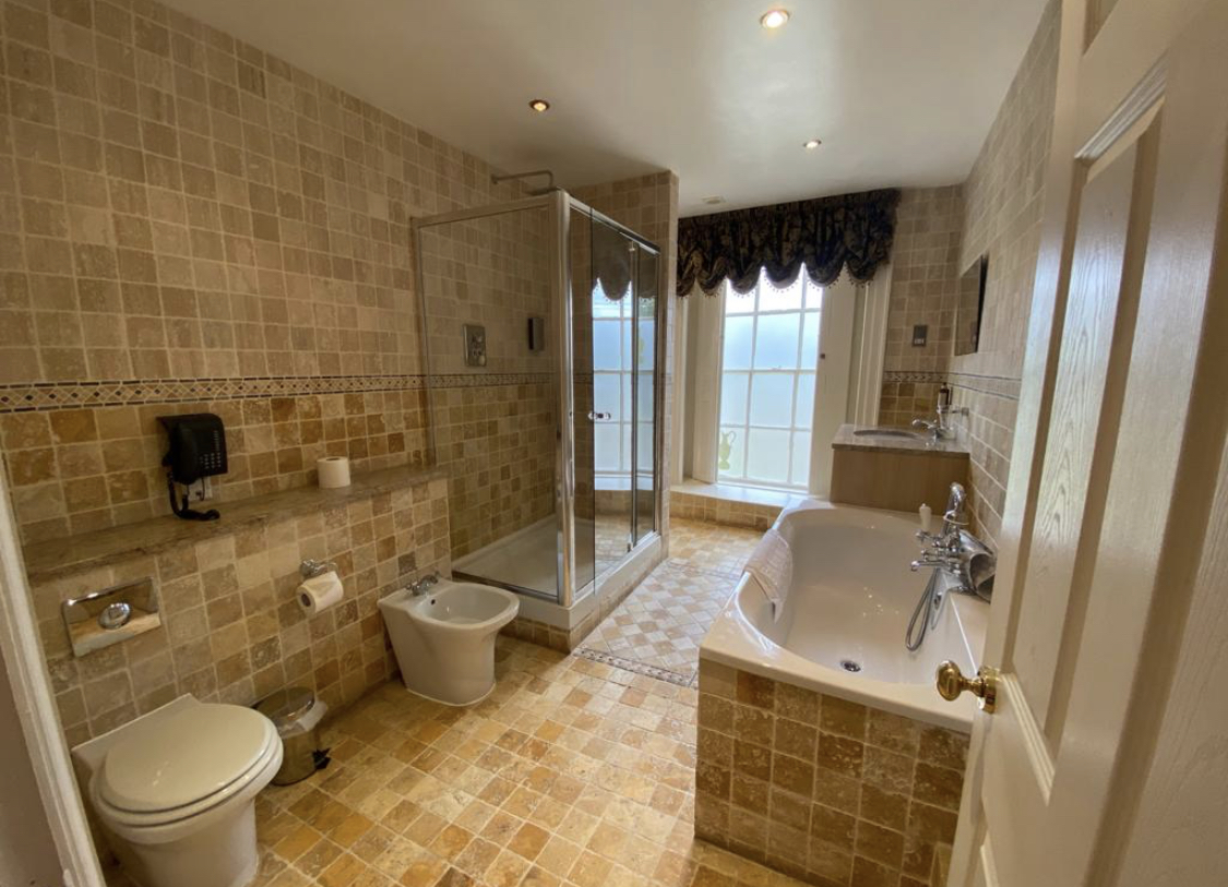 A tiled bathroom showing a toilet, sink, bath tub, bidet and walk in glass shower.