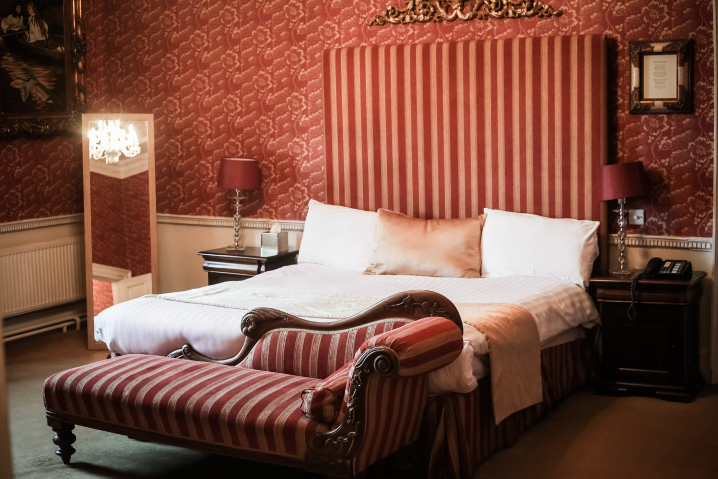 A grand, red bed with a matching sofa in front of it. Two bedside lamps either side.